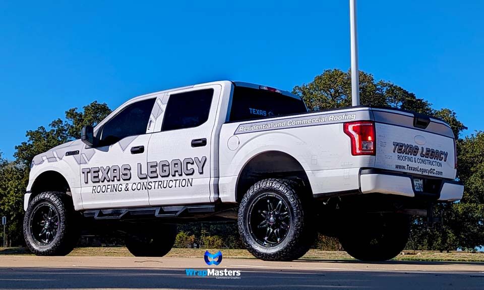 White Ford F-150 Raptor truck with custom "TEXAS LEGACY ROOFING & CONSTRUCTION" wrap, parked outdoors with a clear blue sky and WrapMasters logo watermark.